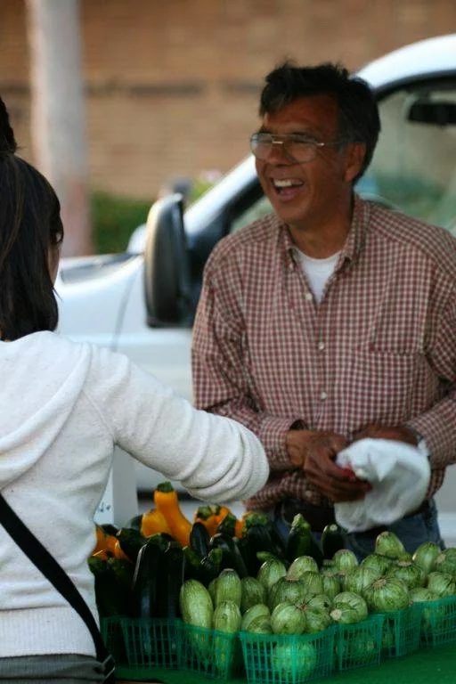 Farmer smiling with a customer over baskets of squash